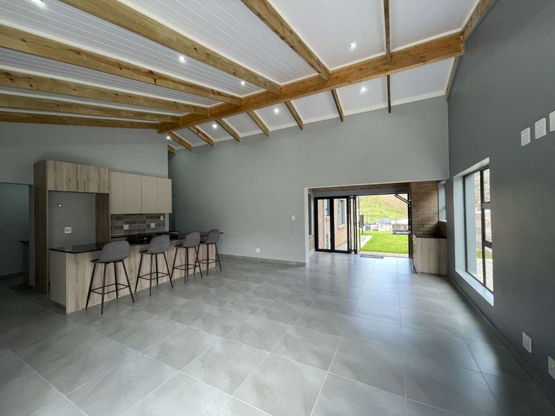 Spacious open-plan living and kitchen area featuring high vaulted ceilings with exposed timber beams, modern tiled floors, and seamless access to the outdoor garden.