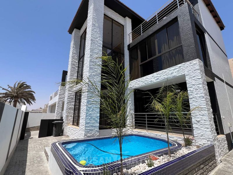 Modern multi-story residence featuring a private swimming pool, stone-clad exterior facade, and upper-level balcony with metal railings.