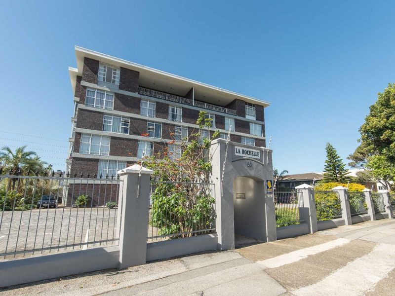 Front exterior view of La Rochelle apartment building featuring a brick facade, secure perimeter fencing, and a gated pedestrian entrance.