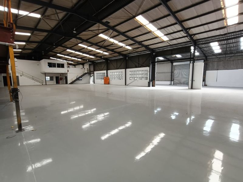 Spacious industrial warehouse featuring a high-clearance steel portal frame, polished epoxy flooring, mezzanine level, and large roller shutter access.