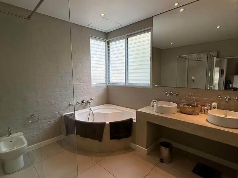 Modern bathroom featuring a corner bathtub, double vanity with vessel sinks, bidet, and a glass-enclosed shower with neutral tiled finishes.