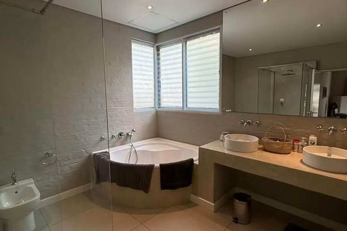 Modern bathroom featuring a corner bathtub, double vanity with vessel sinks, bidet, and a glass-enclosed shower with neutral tiled finishes.