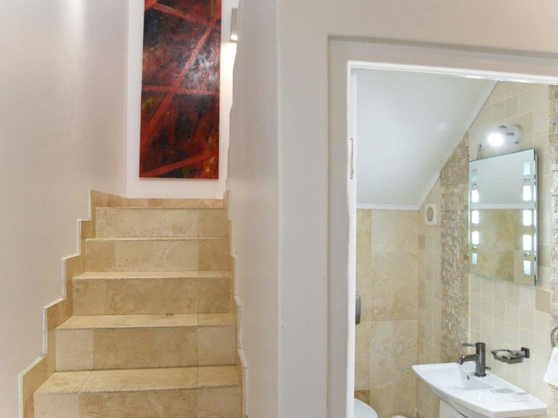 A view of a travertine staircase leading upwards, adjacent to a compact bathroom featuring a pedestal basin and decorative stone wall tiling.