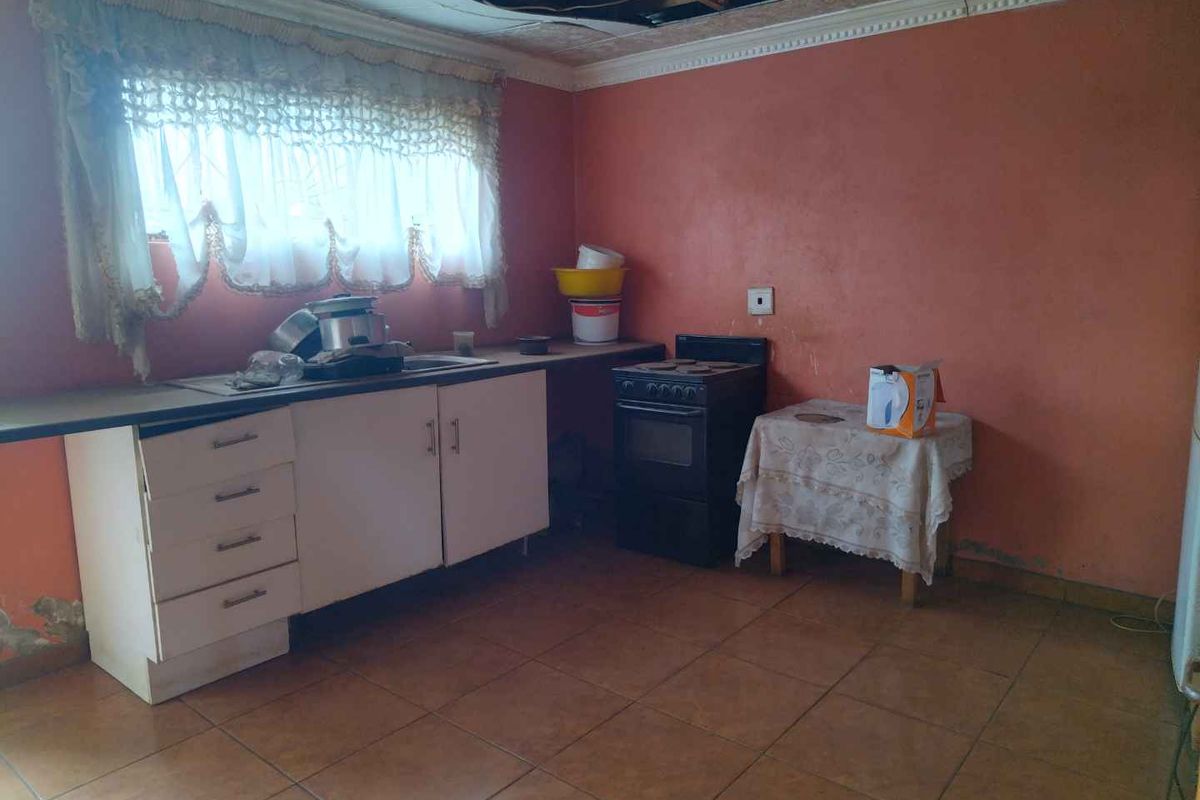 A dated kitchen featuring basic cabinetry, a freestanding stove, and tiled flooring, currently requiring significant renovation and ceiling repairs.