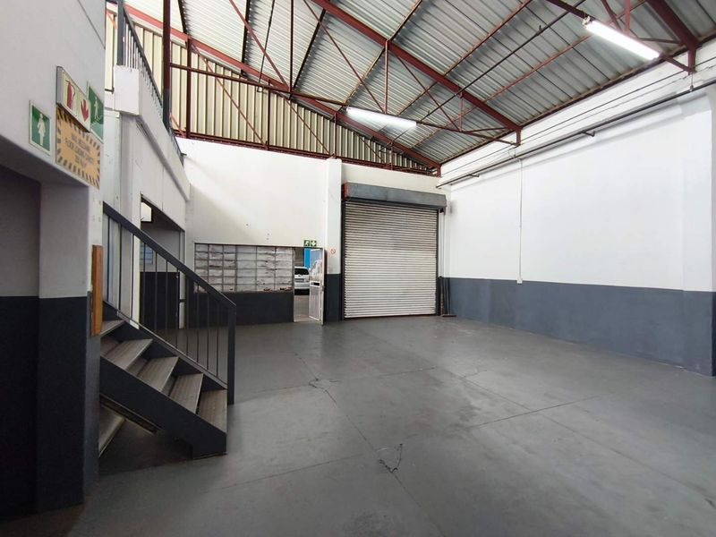 Spacious industrial warehouse unit featuring high ceilings with exposed steel trusses, a large roller shutter door, and durable concrete flooring.