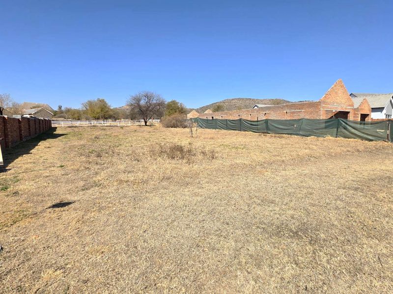 A vacant residential plot featuring a brick boundary wall and construction fencing, offering a clear space for future development.