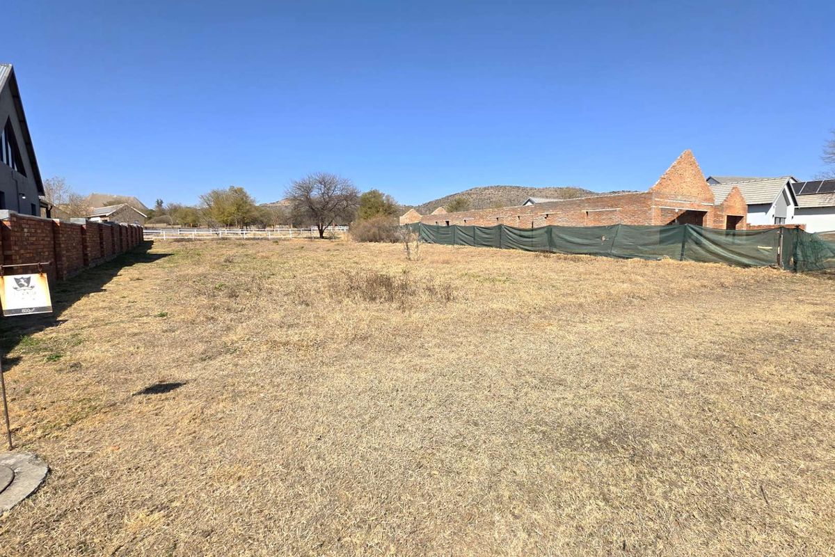 A vacant residential plot featuring a brick boundary wall and construction fencing, offering a clear space for future development.