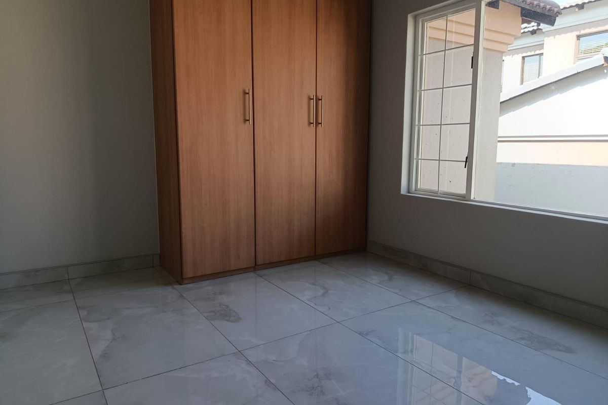 A bright bedroom featuring polished marble-look floor tiles and a built-in wooden wardrobe.