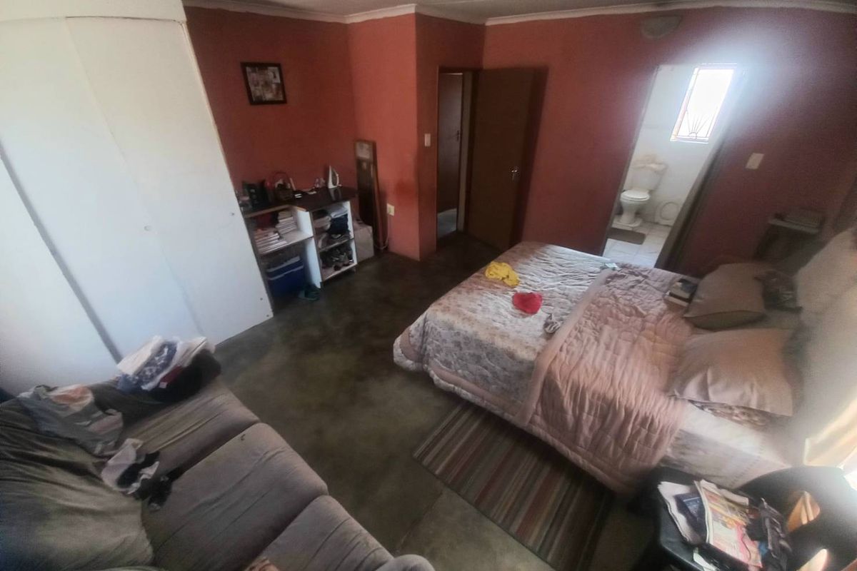 A bedroom featuring a built-in wardrobe and an en-suite bathroom, with concrete flooring and painted walls.
