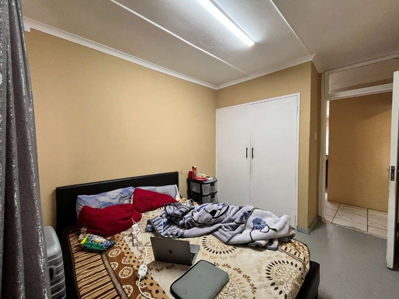 A bedroom featuring a built-in wardrobe and fluorescent lighting, requiring cosmetic updates to the ceiling and wall finishes.