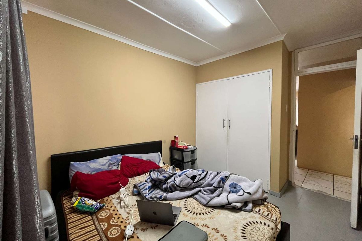 A bedroom featuring a built-in wardrobe and fluorescent lighting, requiring cosmetic updates to the ceiling and wall finishes.