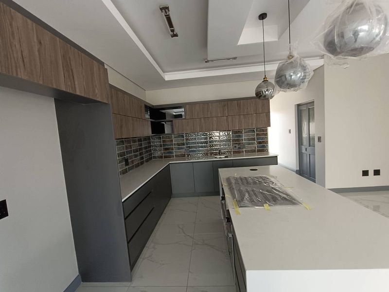 Modern kitchen featuring sleek two-tone cabinetry, stone countertops, a central island, and stylish tiled backsplash, currently in a new, unfinished state.