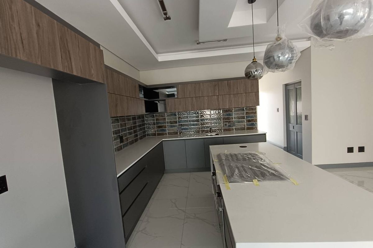 Modern kitchen featuring sleek two-tone cabinetry, stone countertops, a central island, and stylish tiled backsplash, currently in a new, unfinished state.