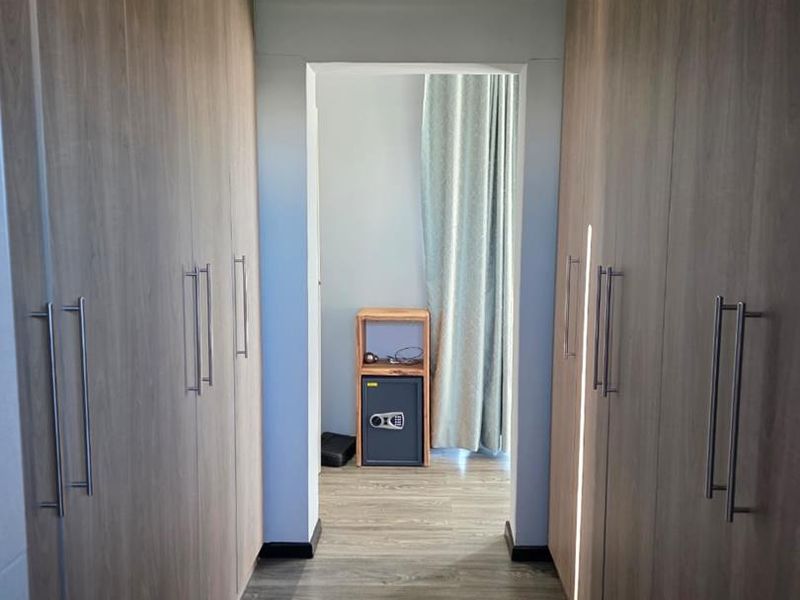 A well-maintained walk-through dressing area or hallway featuring extensive built-in cabinetry with modern wood-grain finishes and durable laminate flooring.