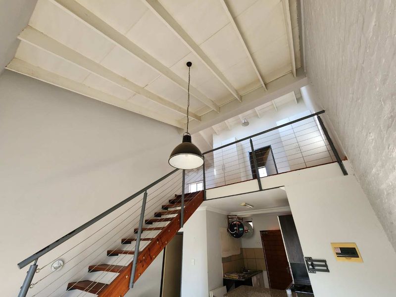 Open plan living area featuring a mezzanine level, exposed beam ceilings, and a steel staircase, offering a unique industrial-style layout with significant renovation potential.