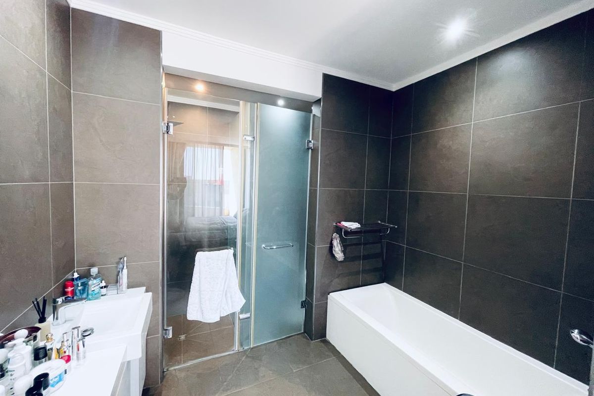 Modern bathroom featuring dark tiled walls, a built-in bathtub, and a separate glass-enclosed shower area with contemporary fixtures.