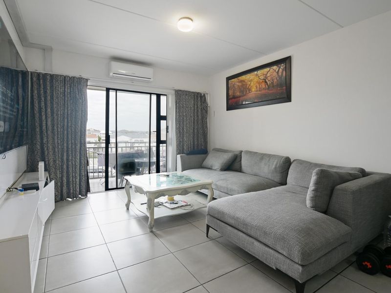 A functional living room featuring ceramic floor tiles, a wall-mounted air conditioning unit, and sliding glass doors providing access to an outdoor balcony.