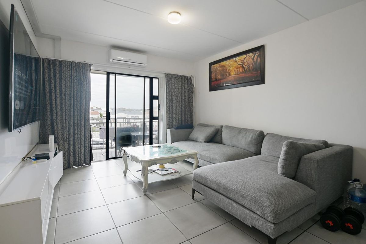 A functional living room featuring ceramic floor tiles, a wall-mounted air conditioning unit, and sliding glass doors providing access to an outdoor balcony.