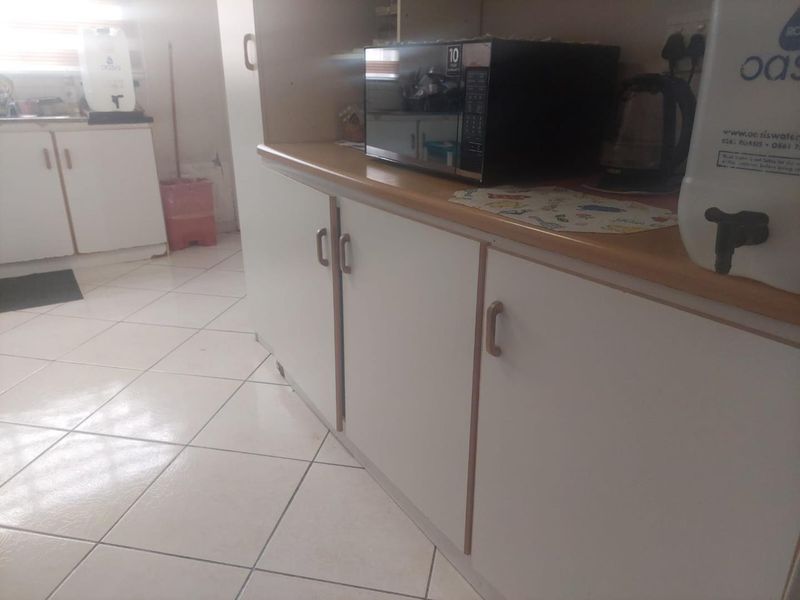 A functional kitchen area featuring white cabinetry, laminate countertops, and ceramic floor tiles, showing signs of wear and dated finishes.