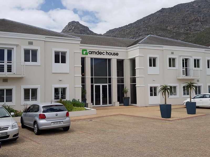Front elevation of Amdec House, featuring a modern double-storey office facade with a prominent glass entrance atrium and paved parking area.
