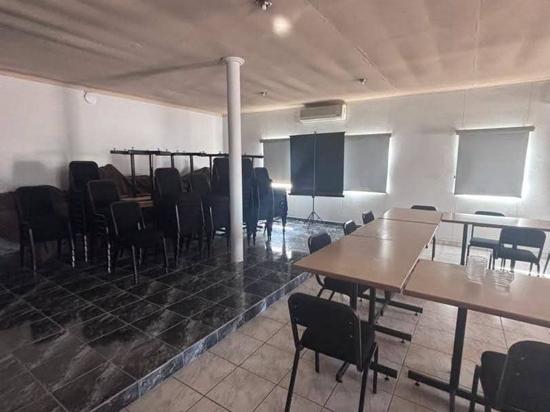 Open-plan commercial space featuring a raised platform area, tiled flooring, split-system air conditioning, and roller blinds on windows.