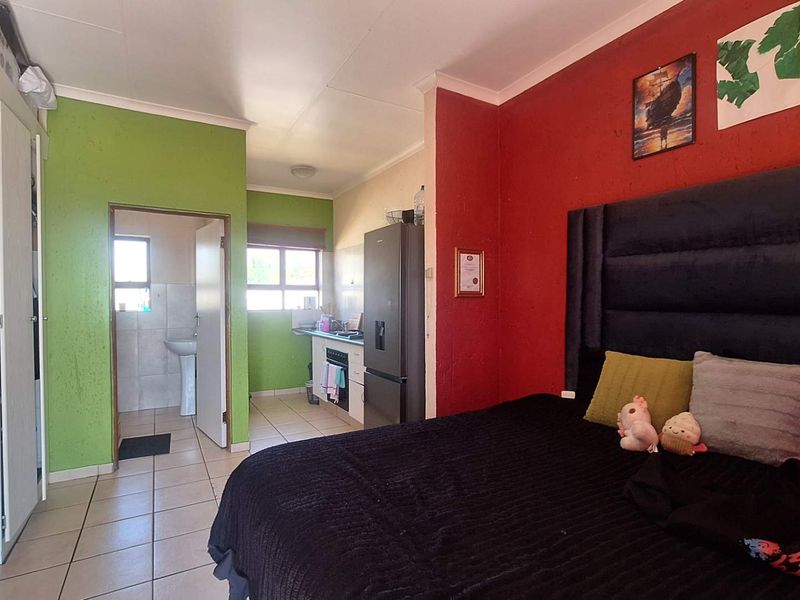 Open-plan bedroom area featuring tiled flooring, integrated storage, and an adjoining kitchenette and bathroom space with a pedestal basin.