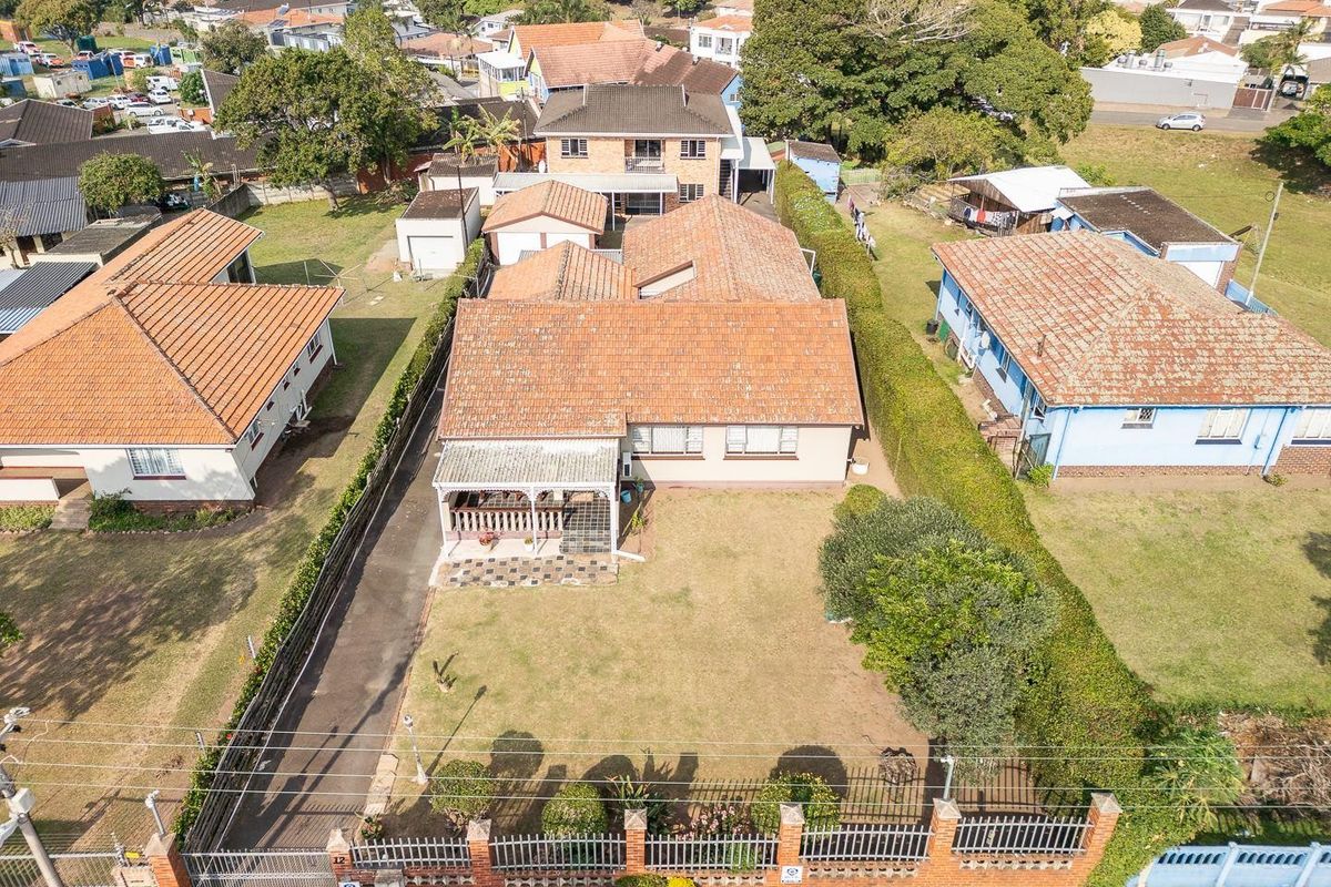 Aerial view of a residential property featuring a tiled roof, a front garden, a paved driveway, and a covered patio area.