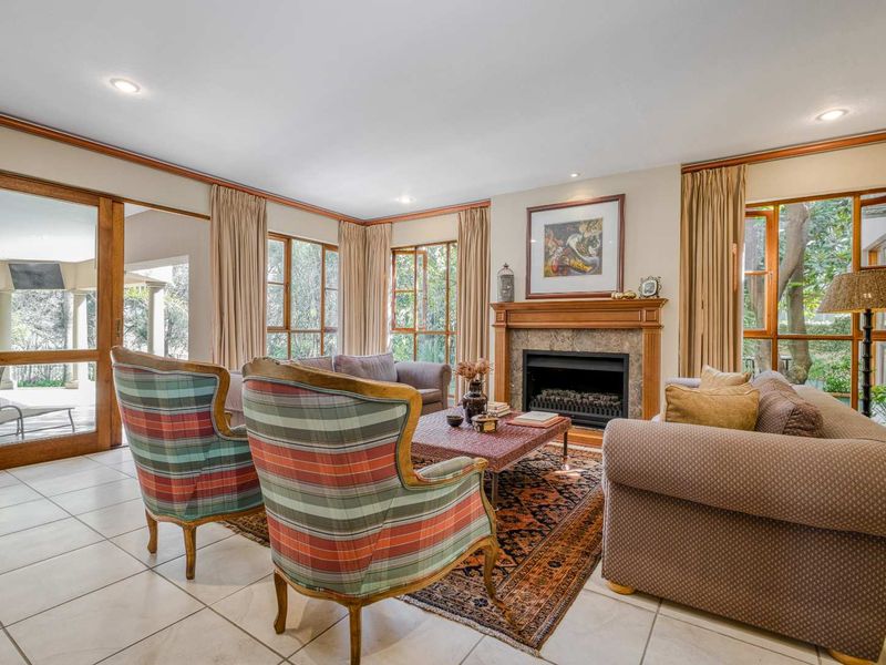 Spacious living room featuring a classic fireplace with a wooden mantelpiece, tiled flooring, and large windows providing natural light and garden views.