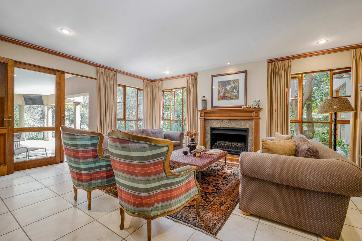 Spacious living room featuring a classic fireplace with a wooden mantelpiece, tiled flooring, and large windows providing natural light and garden views.