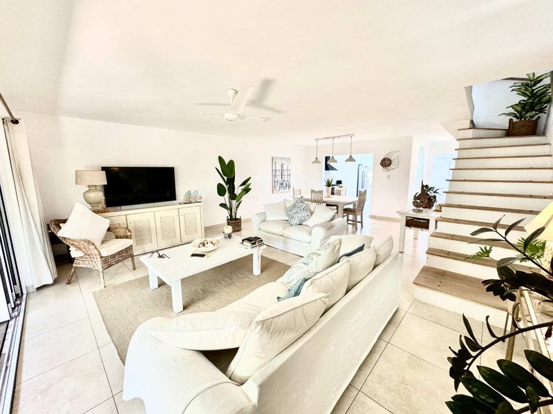 Spacious open-plan living and dining area featuring tiled flooring, a ceiling fan, and a staircase leading to the upper level.