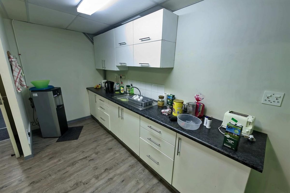 A functional kitchenette area featuring white cabinetry, dark laminate countertops, a stainless steel sink, and wood-look vinyl flooring.