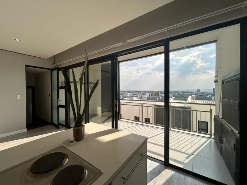 Modern open-plan kitchen area featuring a central island with a built-in hob, flowing seamlessly onto a balcony with a built-in braai and city views.
