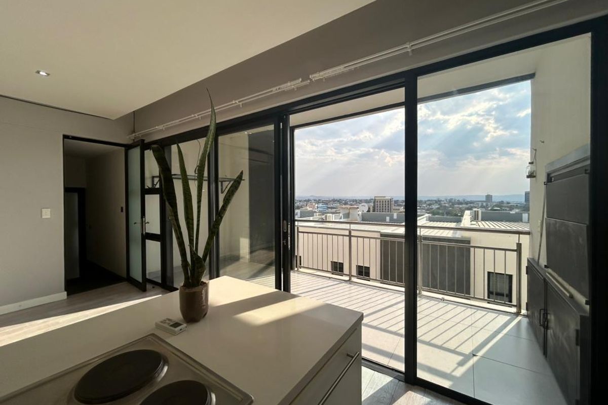 Modern open-plan kitchen area featuring a central island with a built-in hob, flowing seamlessly onto a balcony with a built-in braai and city views.