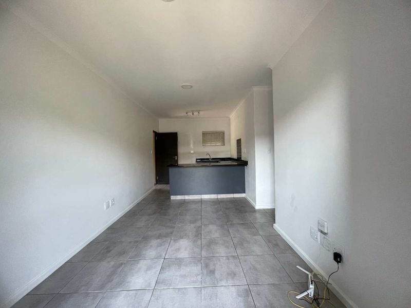 An empty open-plan living and kitchen area featuring neutral tiled flooring, modern cabinetry, and a functional kitchen layout.