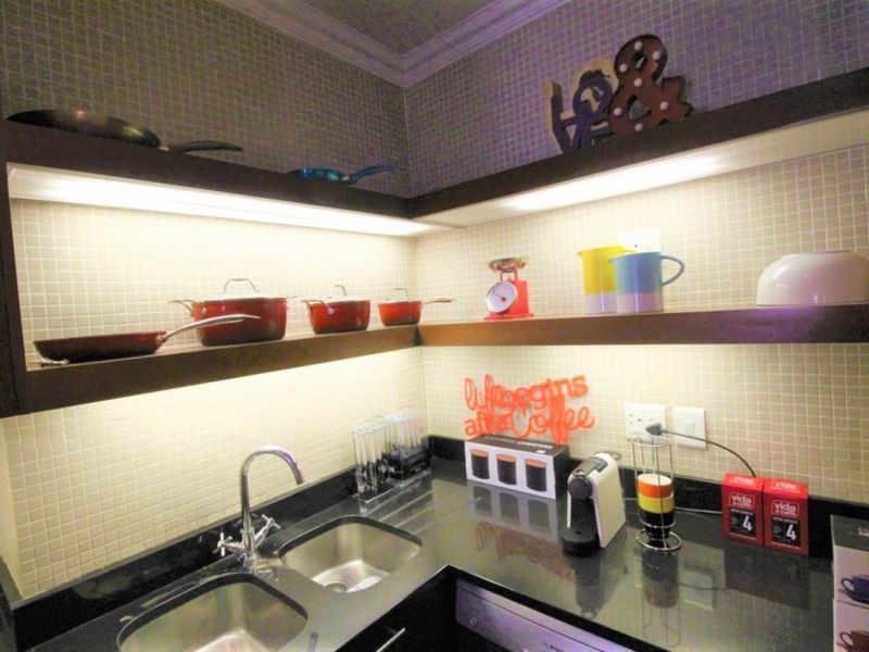 A compact, modern kitchen area featuring granite countertops, a double stainless steel sink, mosaic tile backsplash, and integrated under-cabinet lighting.