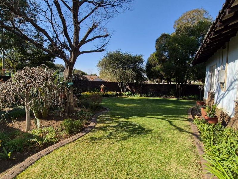 A well-maintained rear garden featuring a lush green lawn, mature trees, and brick boundary walls, providing a private outdoor space.