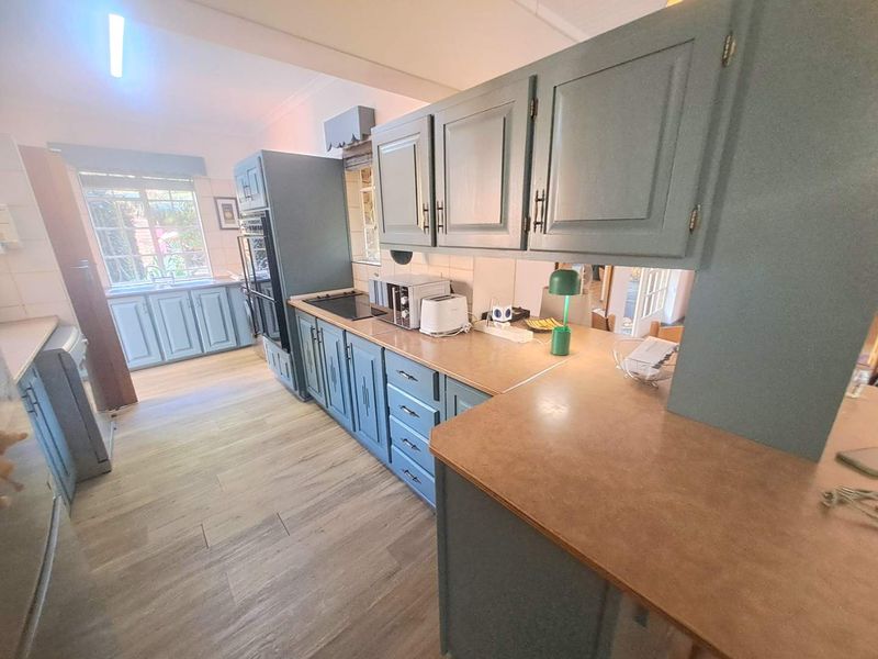 A functional kitchen featuring blue painted cabinetry, laminate countertops, built-in oven, electric hob, and a double sink with wood-look flooring.