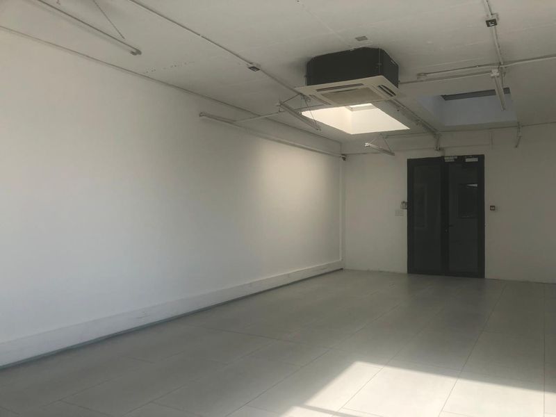 A bright, open-plan office space featuring tiled flooring, a ceiling-mounted air conditioning unit, and a skylight providing natural light.
