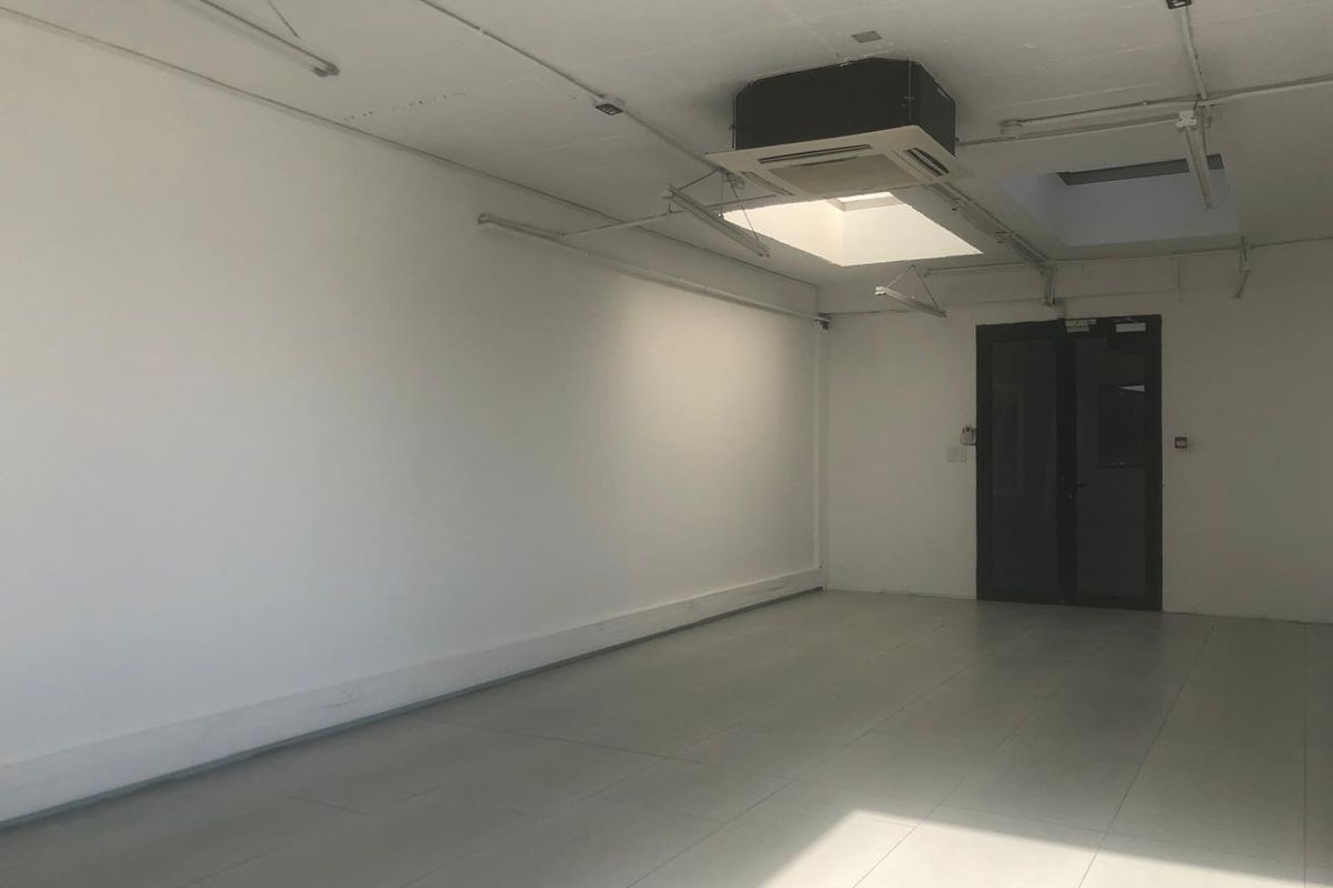 A bright, open-plan office space featuring tiled flooring, a ceiling-mounted air conditioning unit, and a skylight providing natural light.
