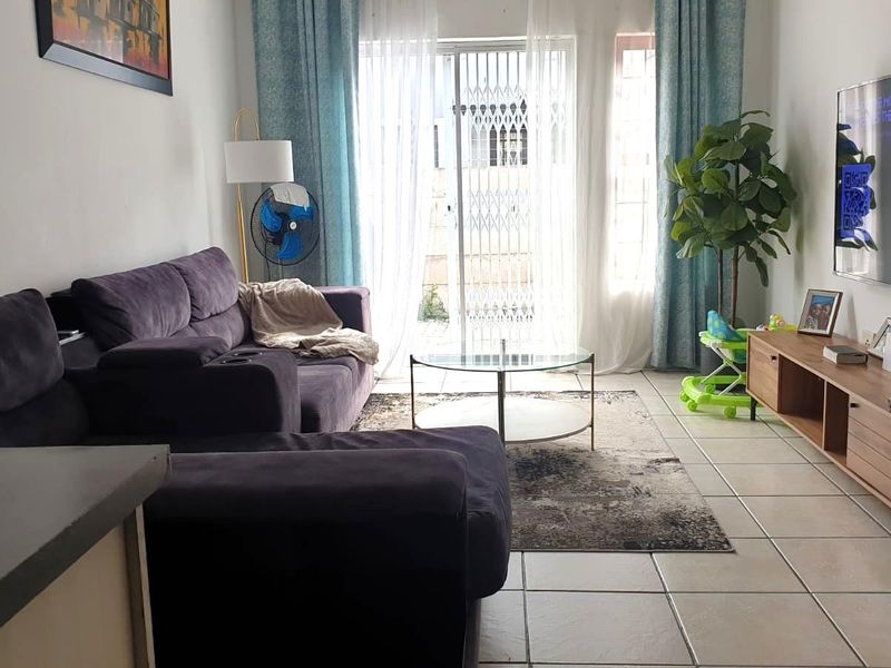 A living room featuring tiled flooring and a sliding glass door with a security gate, providing access to the exterior.