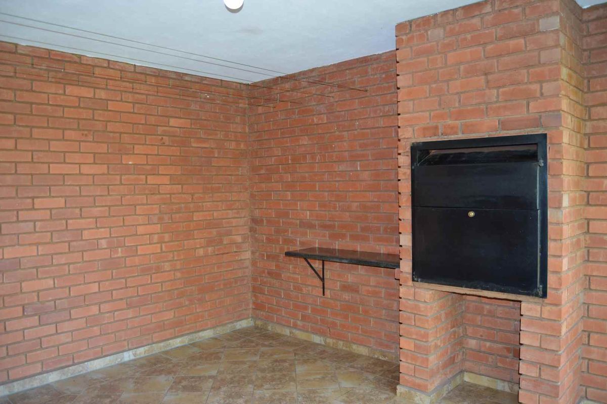 An indoor entertainment area featuring exposed brick walls, tiled flooring, and a built-in brick fireplace with a metal firebox.