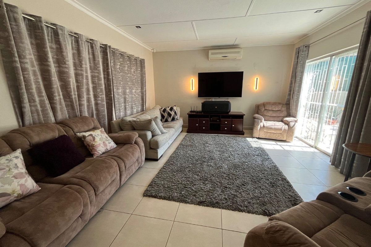 A spacious living room featuring tiled flooring, recessed lighting, wall-mounted air conditioning, and sliding glass doors providing access to the patio.