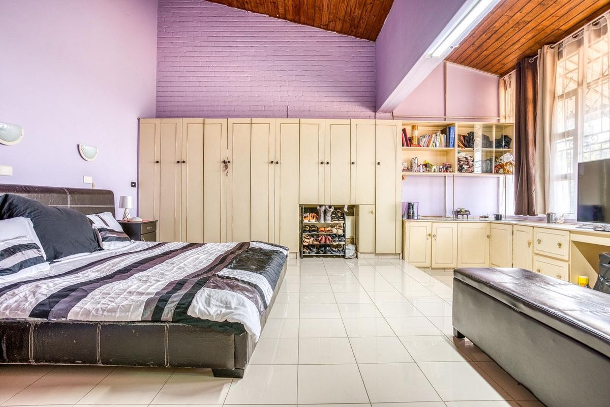 Spacious bedroom featuring high timber ceilings, extensive built-in cabinetry, tiled flooring, and an exposed brick feature wall.