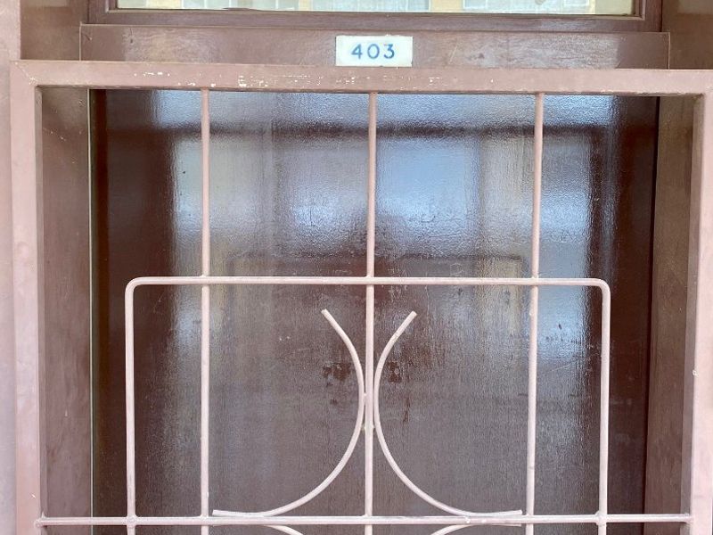 A secure apartment entrance door featuring a brown finish, a transom window above, and a decorative metal security gate.