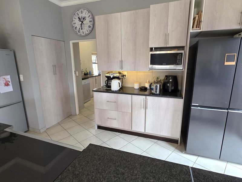 A functional kitchen featuring light wood-finish cabinetry, dark granite countertops, built-in microwave, and tiled flooring, with an adjacent scullery area visible.
