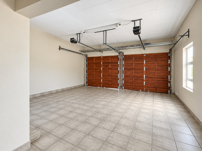 Spacious, clean double garage featuring tiled flooring, automatic wooden doors, and well-maintained finishes.
