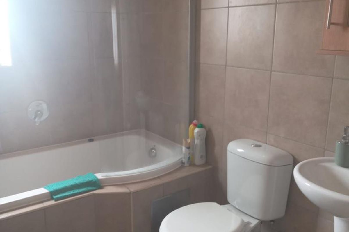 A functional bathroom featuring a built-in bathtub with a glass screen, pedestal basin, and neutral ceramic wall and floor tiling.