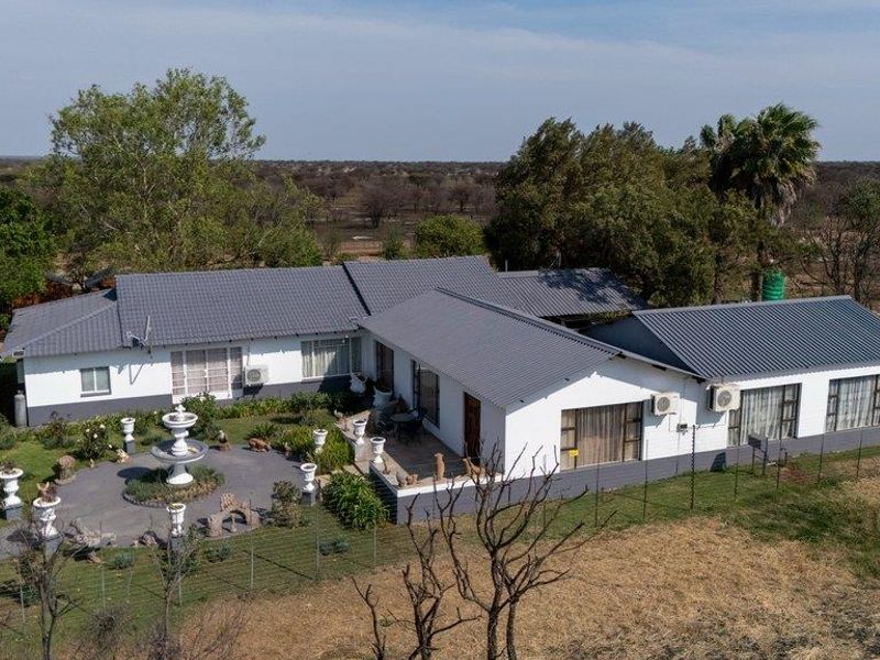 Aerial view of a well-maintained farm residence featuring a tiled roof, paved patio area, and surrounding landscaped grounds.