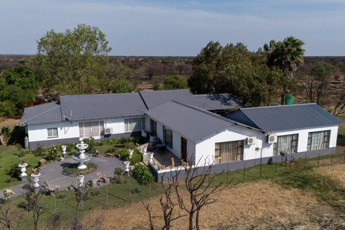 Aerial view of a well-maintained farm residence featuring a tiled roof, paved patio area, and surrounding landscaped grounds.