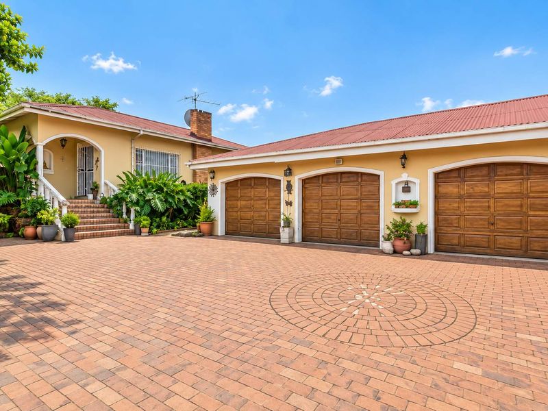 A well-maintained front exterior featuring a spacious brick-paved driveway, a triple garage with wooden doors, and an inviting covered entrance porch.